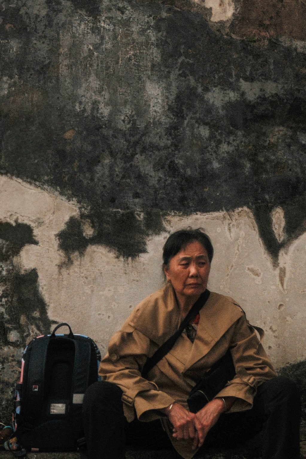 Woman seated beside a backpack against a weathered wall in China photographed by Nick DiBari