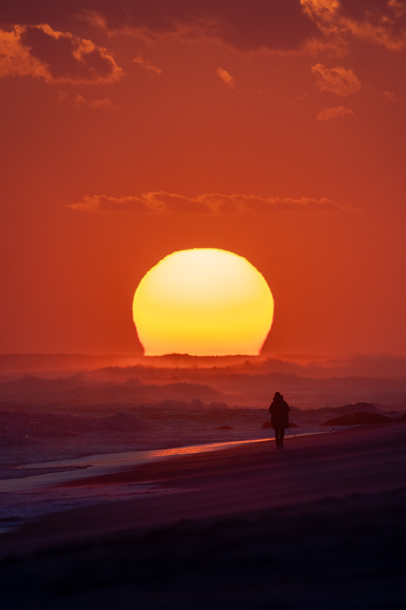 Orange sun setting over the ocean with a person silhouette photographed by Nick DiBari